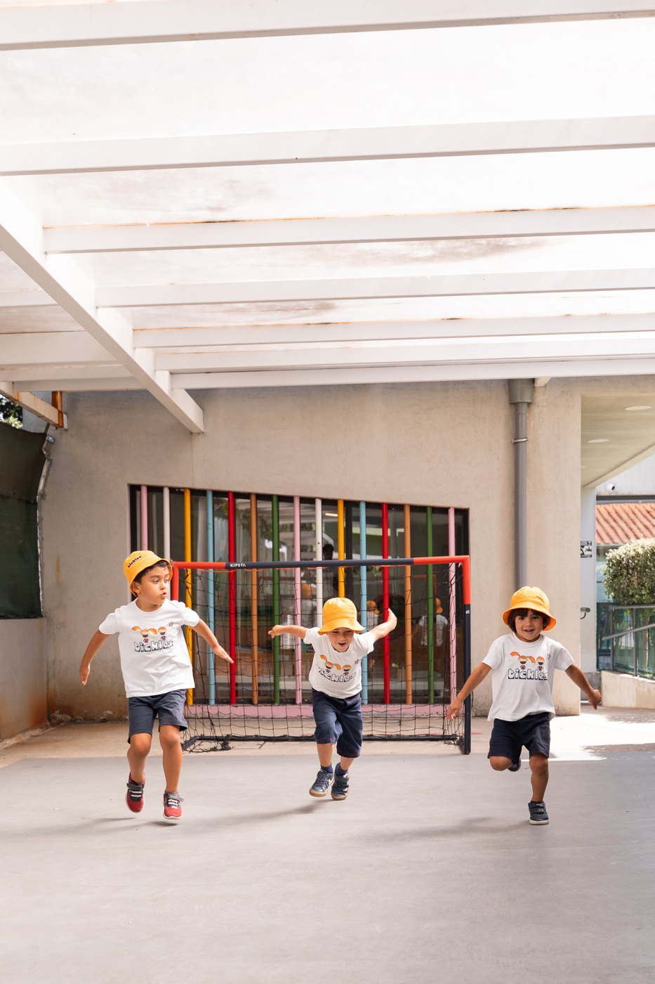 Três crianças a correr de braços abertos no recreio